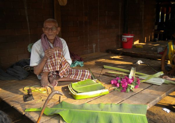Cambodian man surrounded by large bright green leaves and pink flowers