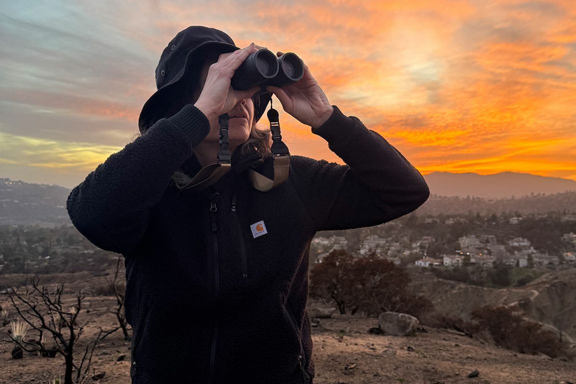 Kristen Ochoa looks through binoculars as she stands in Eaton fire burn scar