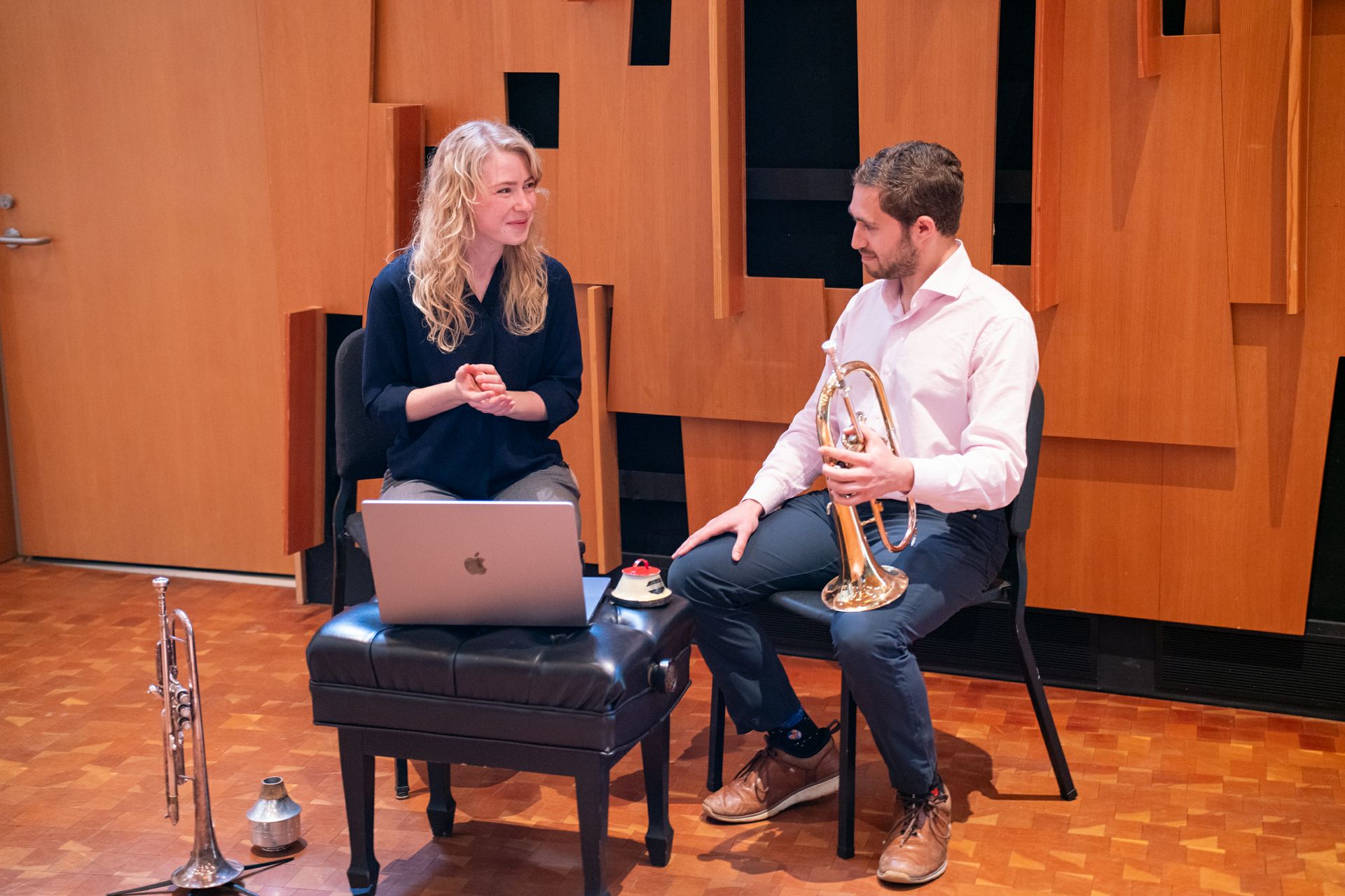 Katie Osborn and Austin Ali seated; Ali holds a horn, and both sit in front of a laptop computer