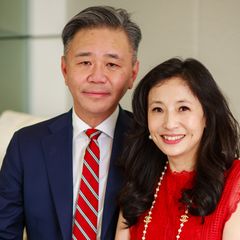 Walter and Shirley Wang pose together, smiling. Walter wears a navy suit with a red striped tie; Shirley wears a red sleeveless top and a pearl necklace.