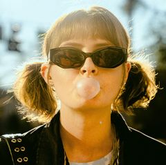 Close-up of woman with pigtails and sunglasses blowing a bubble with gum
