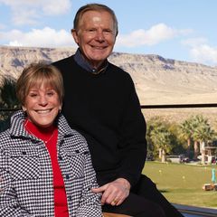 Heidi Canarelli, left, in red, black and white, next to Larry Canarelli, in black sweater, with golf course, palm trees and mountains in background