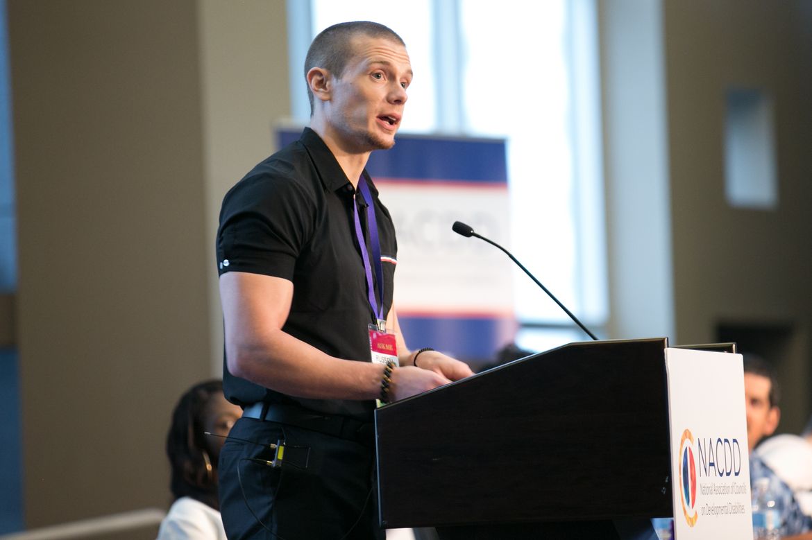 Russell Lehmann in a black polo standing and speaking from a podium. 