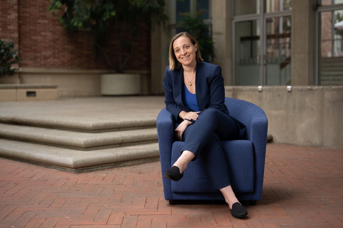 Claire Chaumont, in blue suit, sitting in a blue chair outside a building  