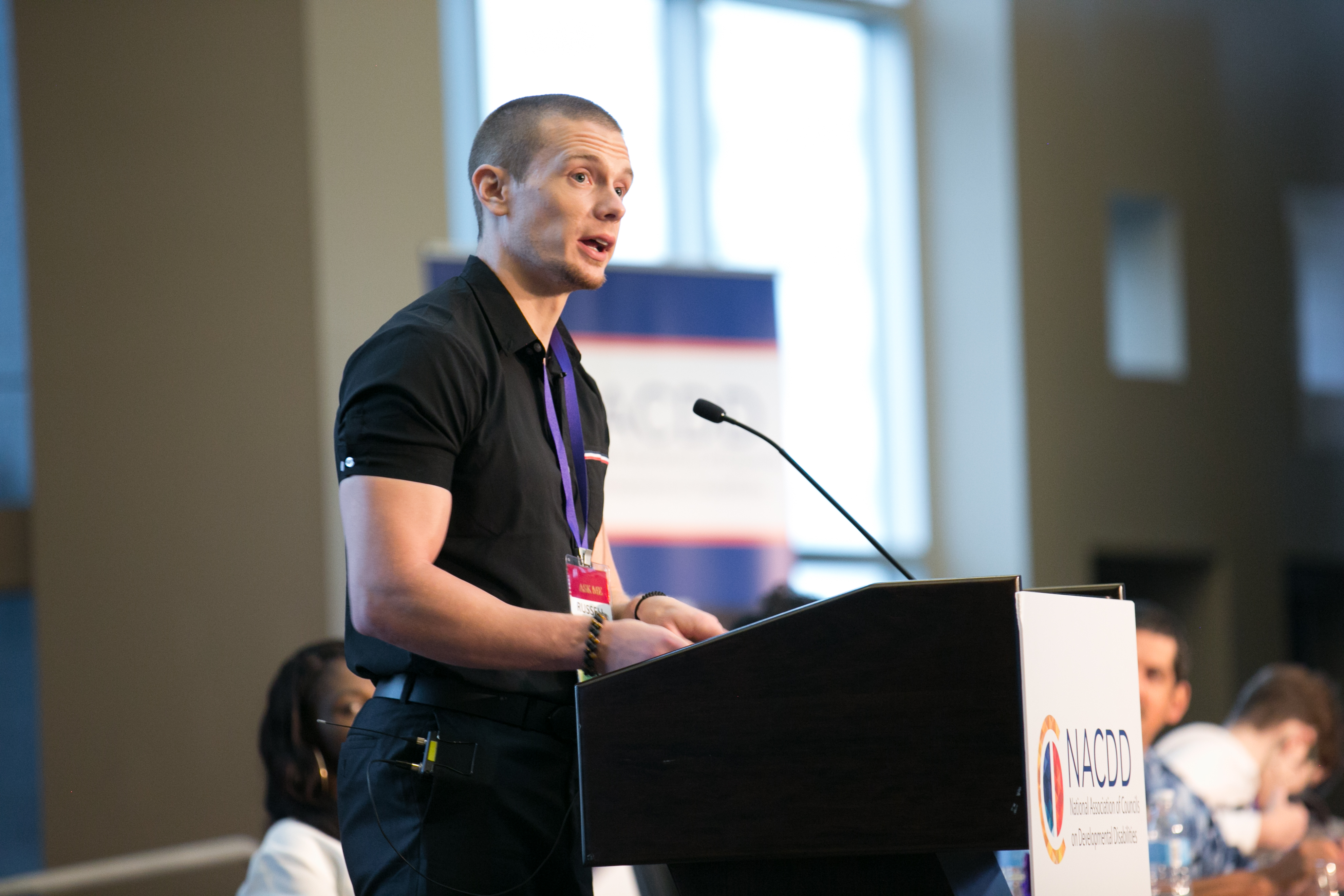 Russell Lehmann in a black polo standing and speaking from a podium