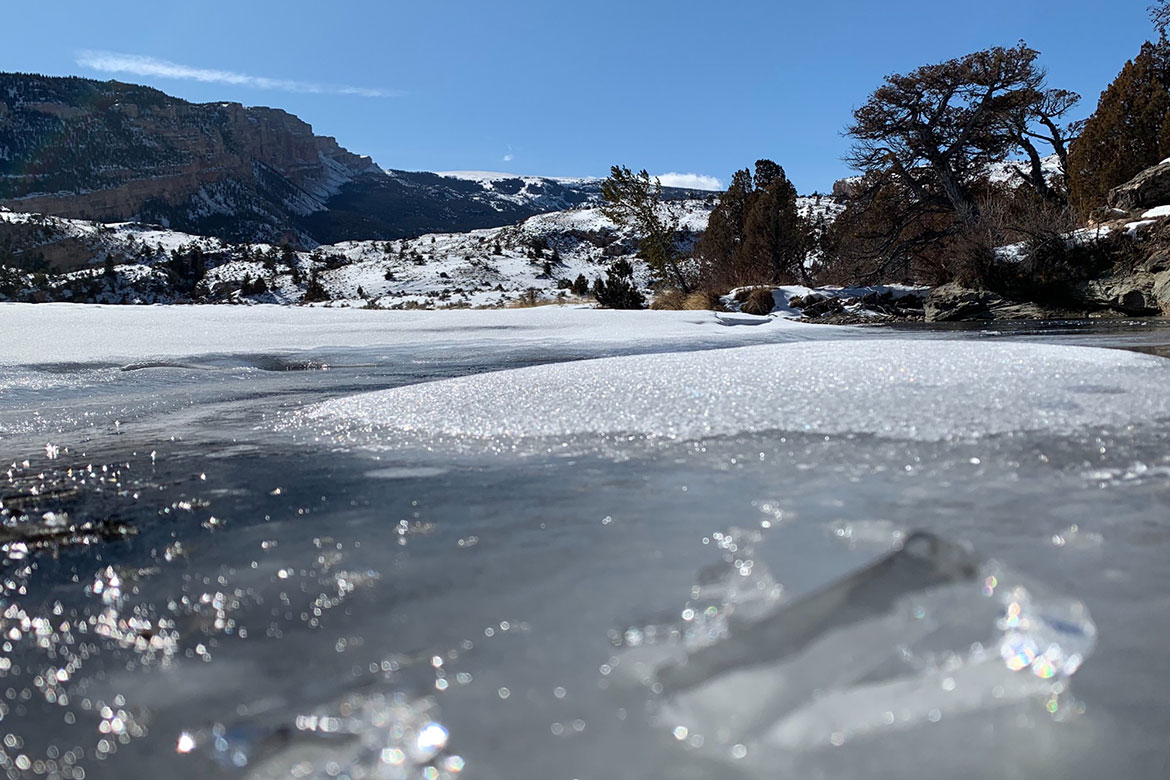 Close-up of river running with some frozen ice in the center and mountains in the background