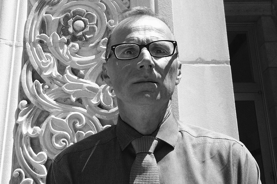 Head-and-shoulders photo of Robert Gurval, in shirt and tie, in front of ornate building decor