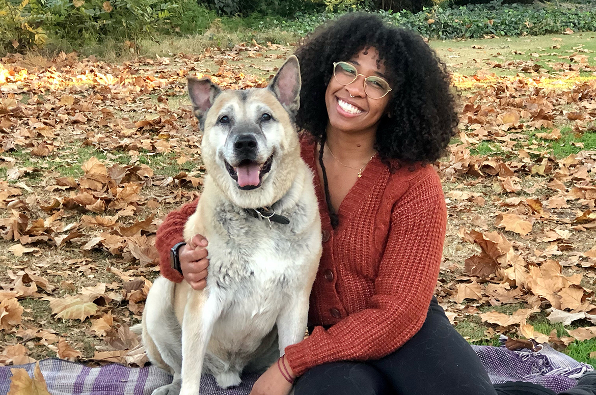 Keo Vutheikun, in brown sweater, sits outdoors on blanket with arm around a white-and-tan dog