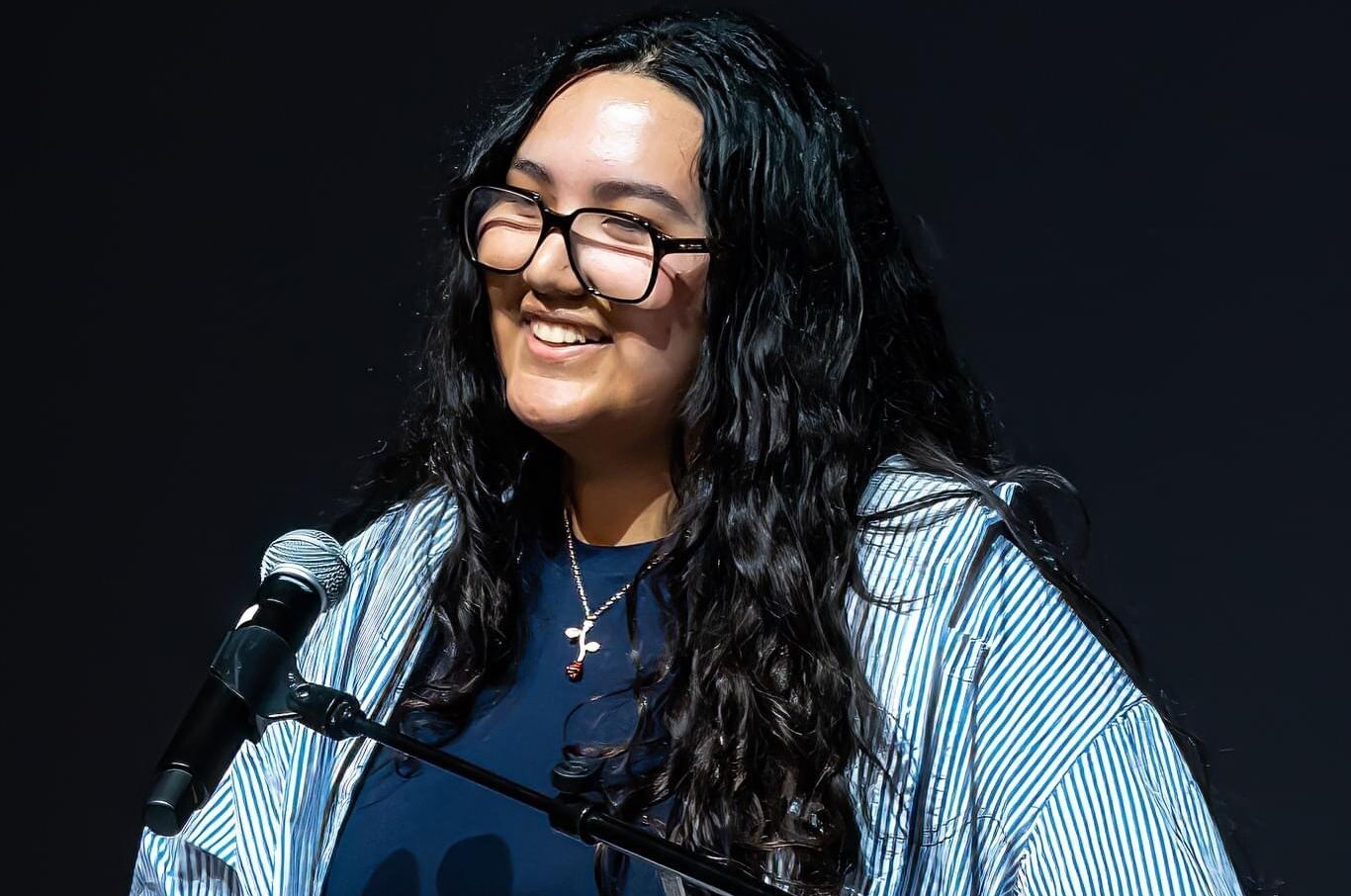 Natalia Zeledon, in blue shirt and striped top, smiles in front of a microphone