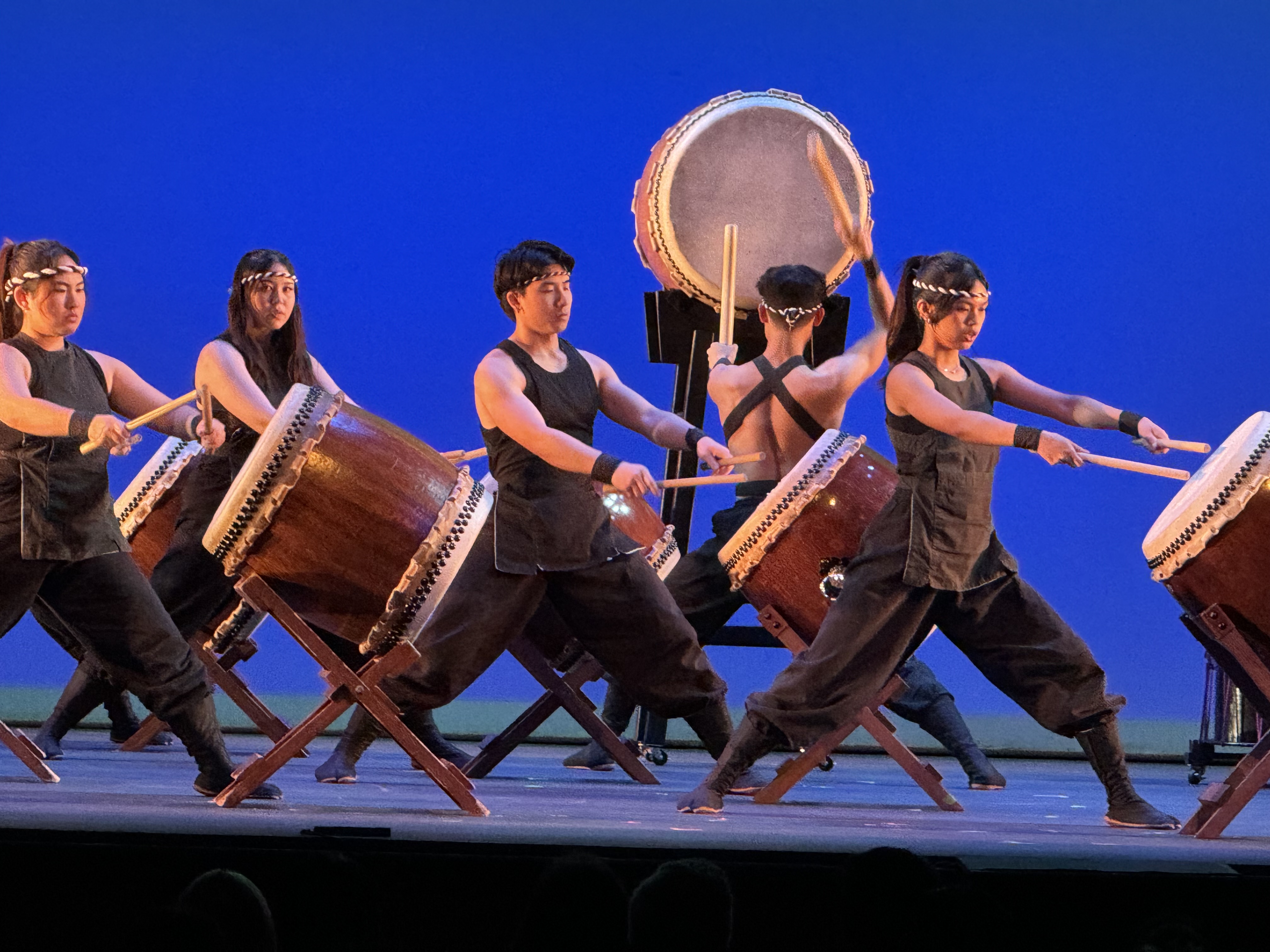 Five taiko drummers performing onstage in front of blue background