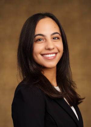 Verna Halim in a black suit jacket posing for a headshot against a light brown backdrop