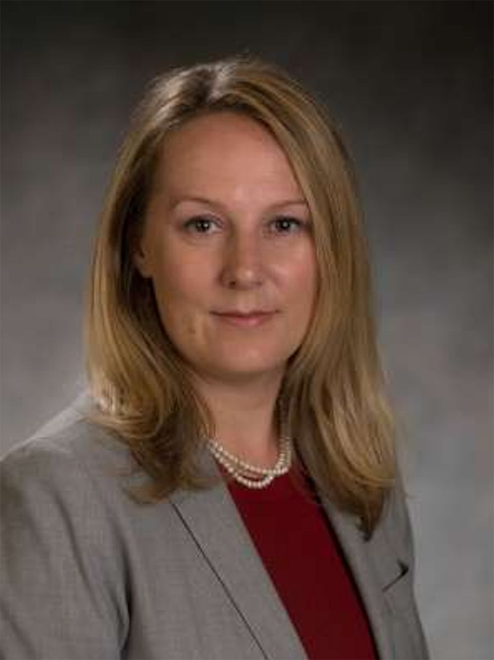 Head-and-shoulders image of Kara Calkins wearing burgundy top, gray jacket and pearl necklace