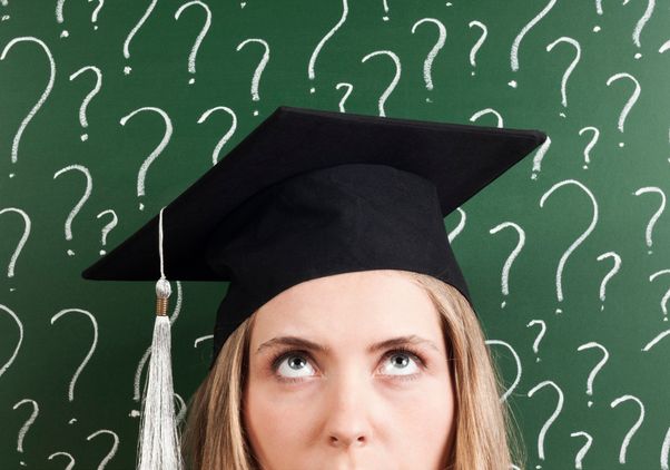 A young female student wearing cap thinking about her future in front of question marks written on a blackboard