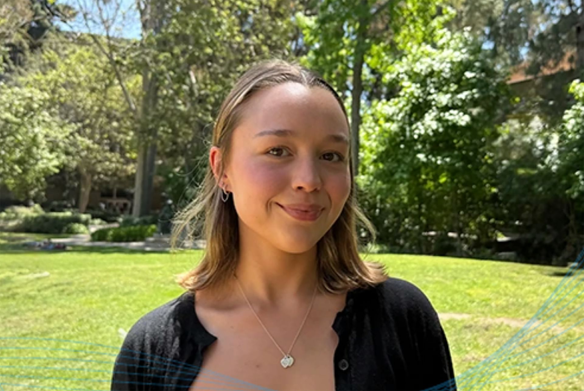 Headshot of Clara Prideaux smiling outdoors on a green UCLA campus lawn, wearing a black cardigan and silver necklace.