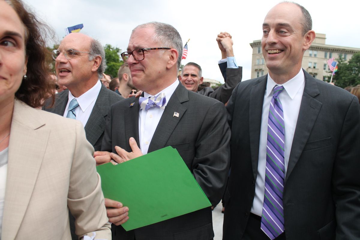 James Obergefell, wearing a bow tie and flag pin and holding a green folder, reacts emotionally alongside his attorney Al Gerhardstein and others in a crowd outside the Supreme Court on June 26, 2015, the day of the marriage equality ruling.