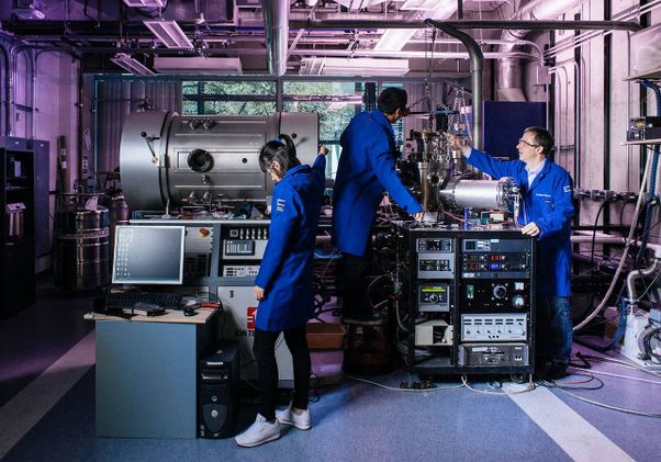 Scientists in blue coats working with machinery in a lab