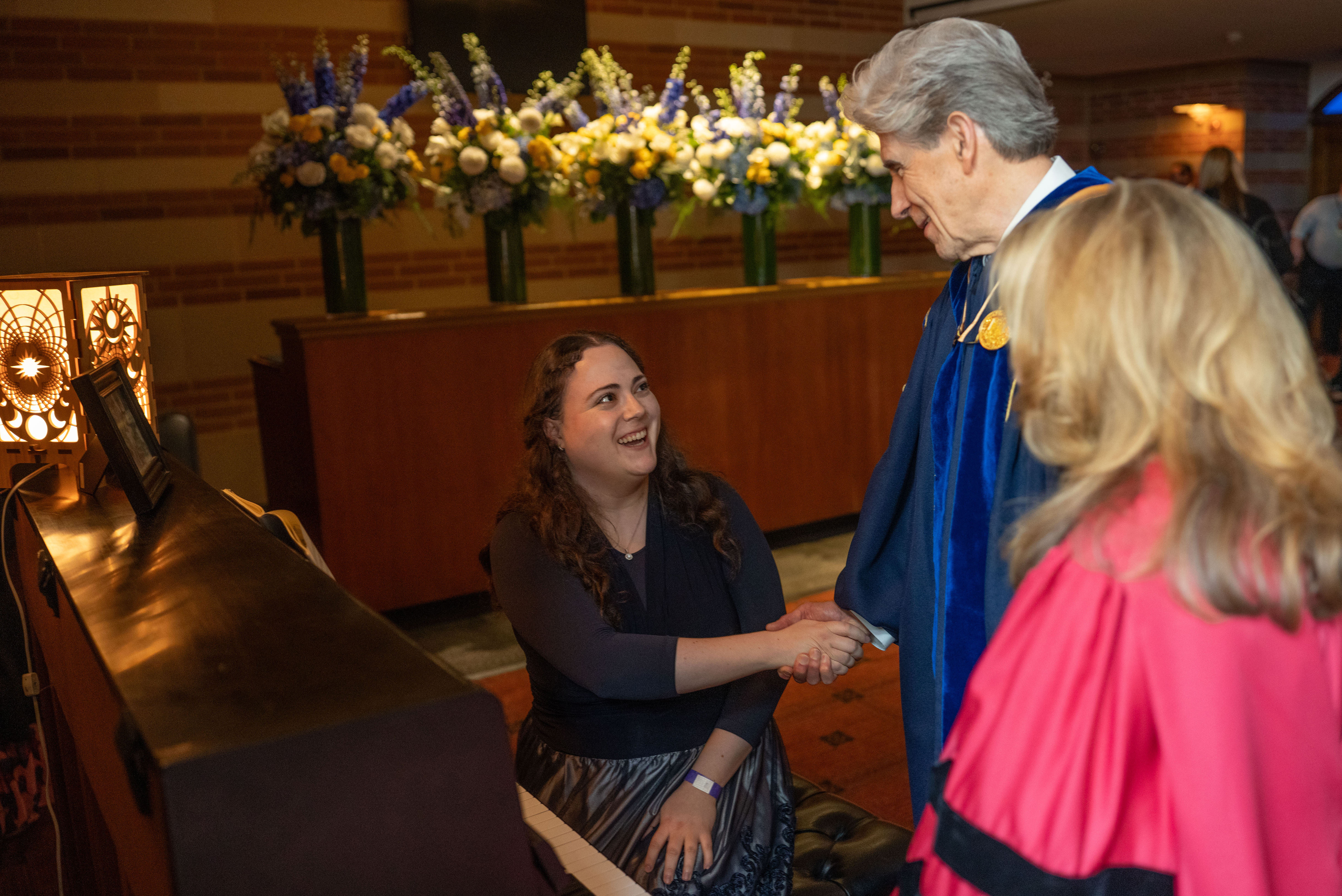 Gabrielle Sipen, seated at piano, shaking hands with Julio Frenk while Felicia Marie Knaul looks on