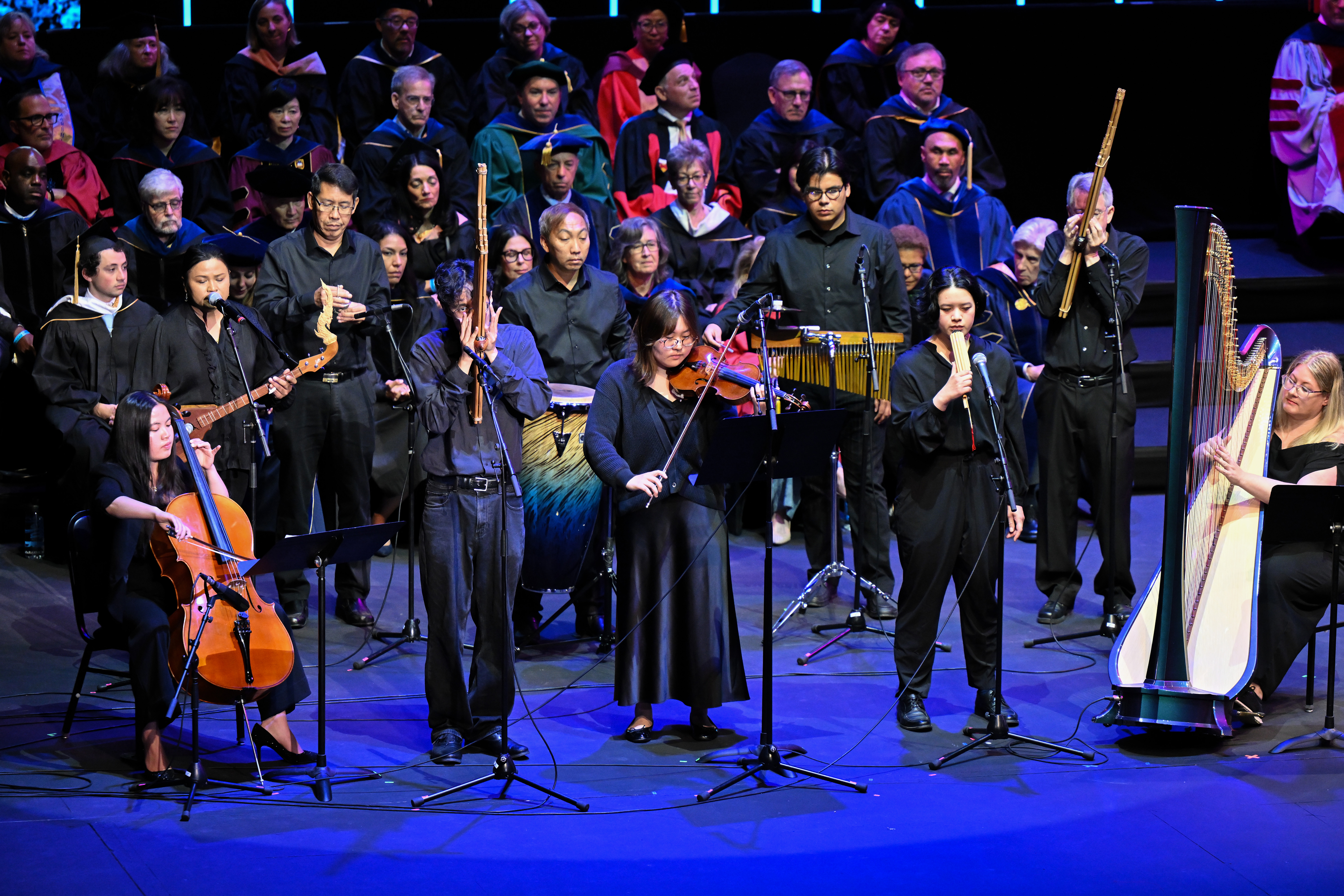 Group of musicians wearing dark blue play various instruments onstage