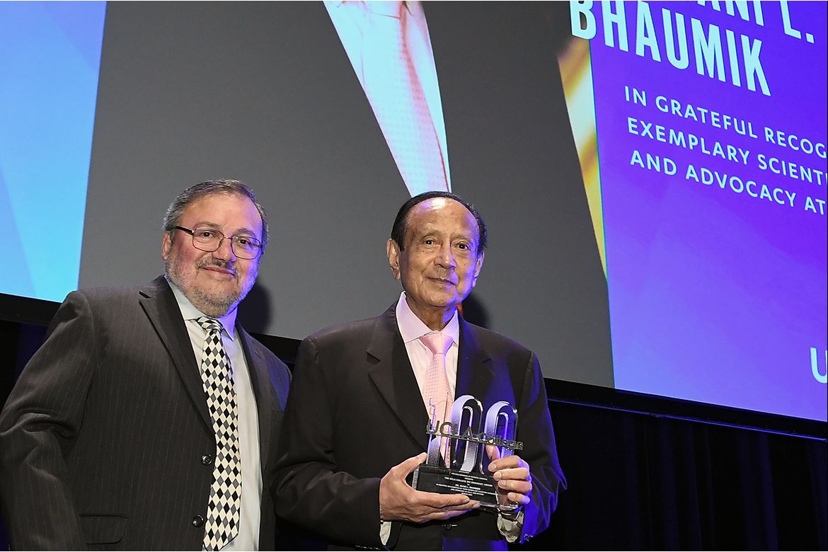 Miguel García-Garibay, left, in black jacket and diamond-patterned tie, and Mani Bhaumik, in black jacket and pink tie, holding a UCLA College 100 trophy