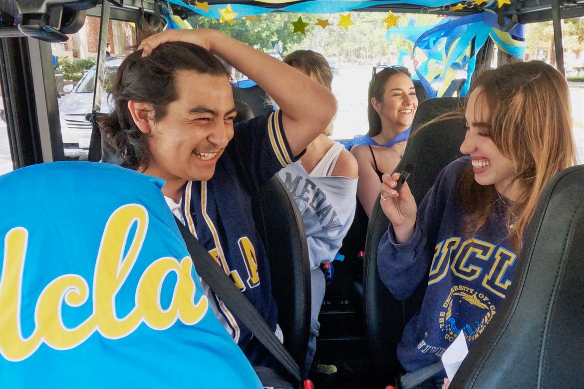 Four students smile as they sit in a golf cart with UCLA script logo covering the front seat