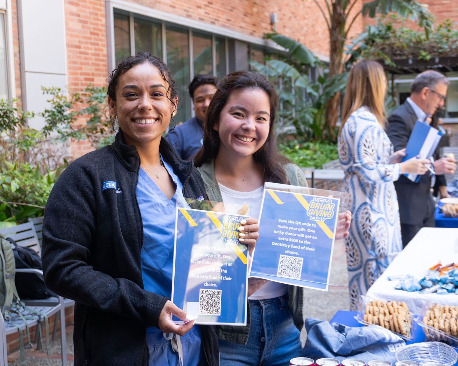 Two dentistry students smiling and holding up Bruin Giving Day signs