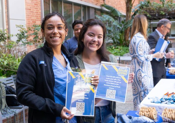 Two dentistry students smiling and holding up Bruin Giving Day signs