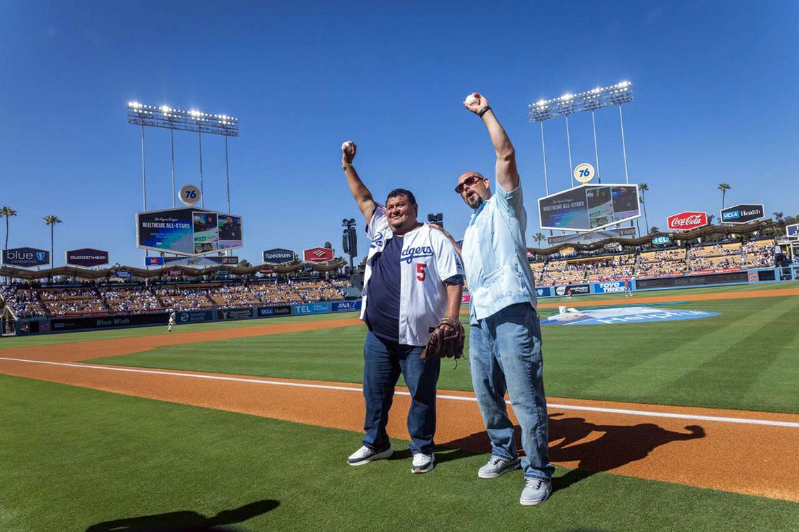 Two men appear on the baseball diamond at Dodger Stadium, each one holding a ball in the air.