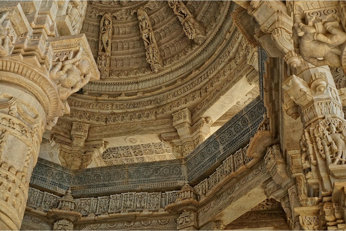 Interior shot of a temple ceiling covered in intricate stone carvings. The ceiling features concentric rings of detailed sculptural relief work, including human and deity figures.