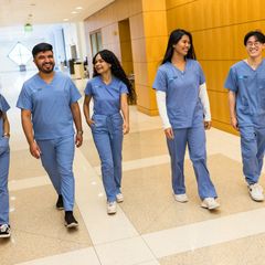 Several UCLA School of Nursing students in scrubs walk down hallway at UCLA