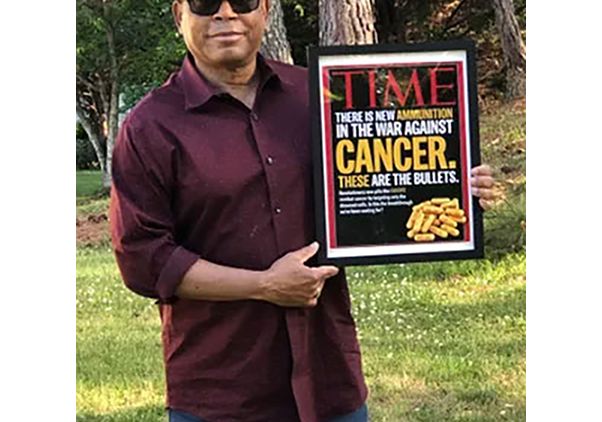 Melvin Mann, in burgundy button-down and straw hat, holding framed Time magazine cover