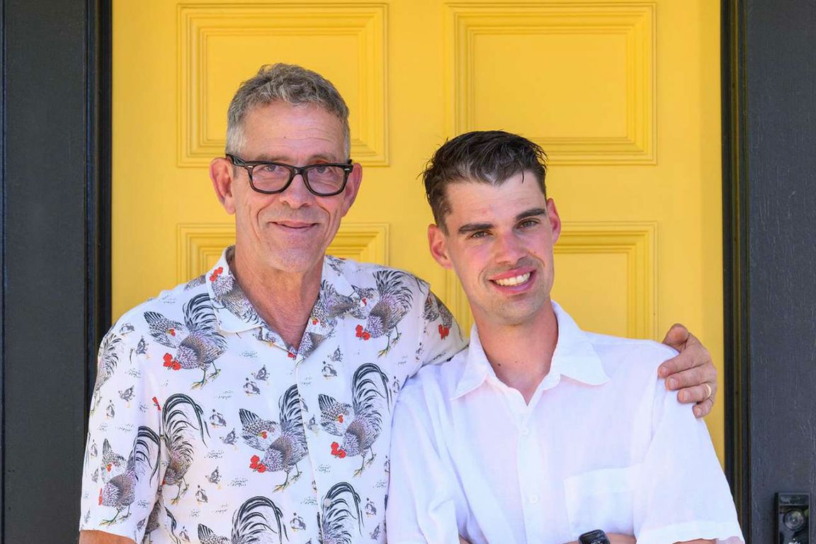 Midrange photo of Joe Henry, in rooster-pattern shirt, with arm around his son, Franklin, in front of a yellow door