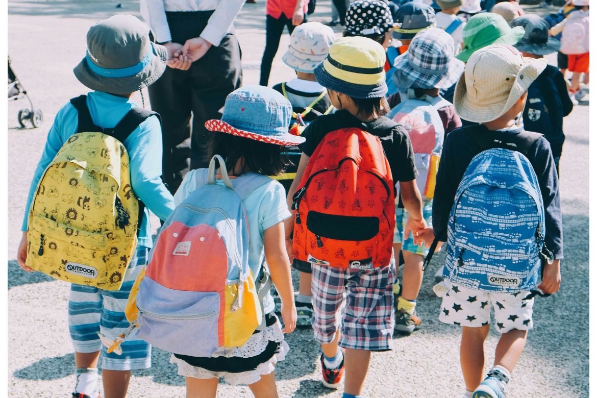 Group of school students wearing white and orange backpacks walking on gray pavement during daytime 