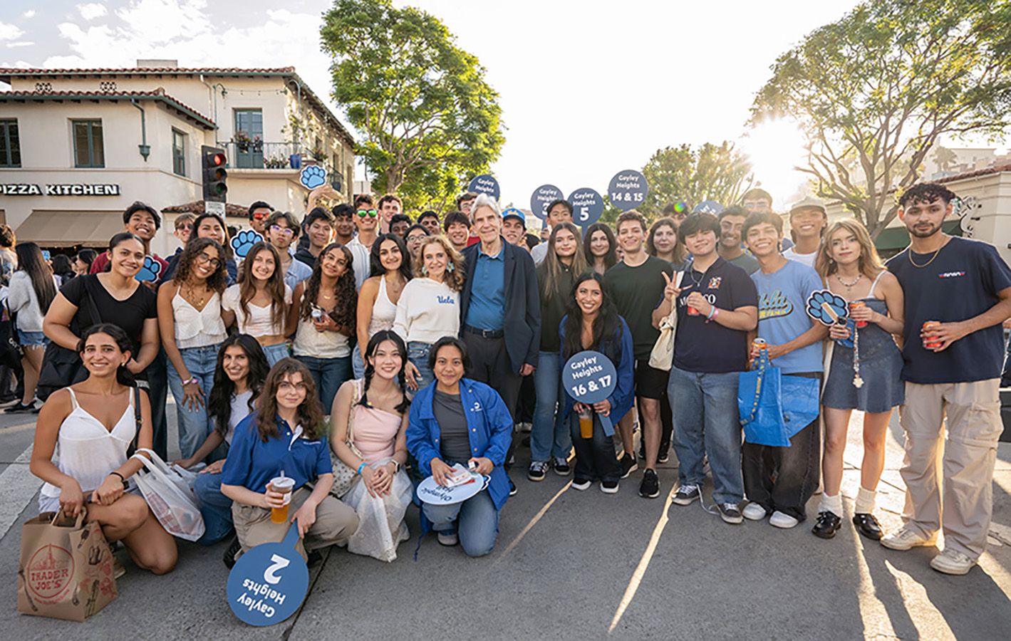 UCLA Chancellor Julio Frenk stands at the center of a large group of smiling new students gathered on a Westwood street for the True Bruin Welcome block party.