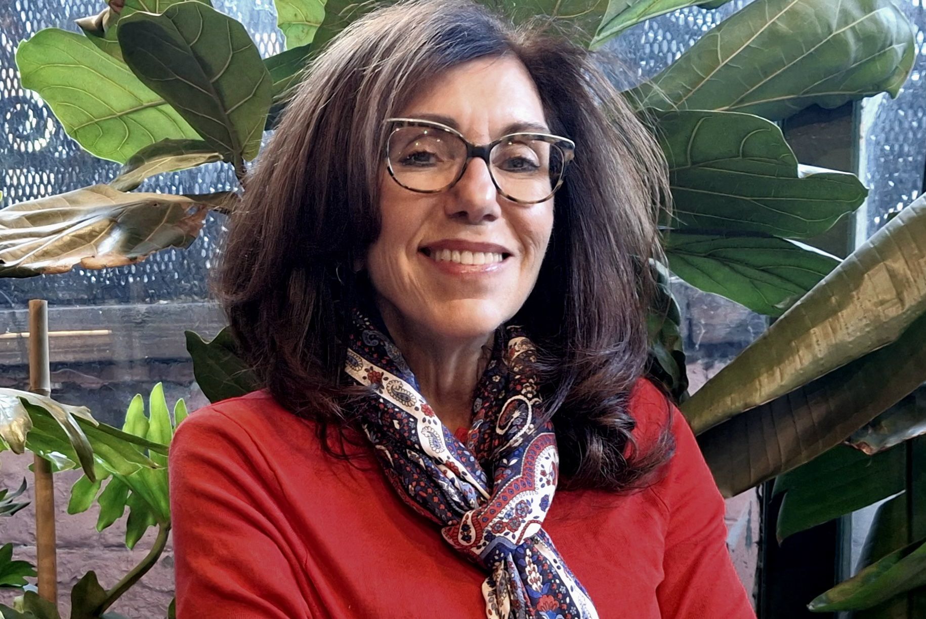 Head-and-shoulders shot of Carol Bakhos wearing red top, silk scarf and glasses