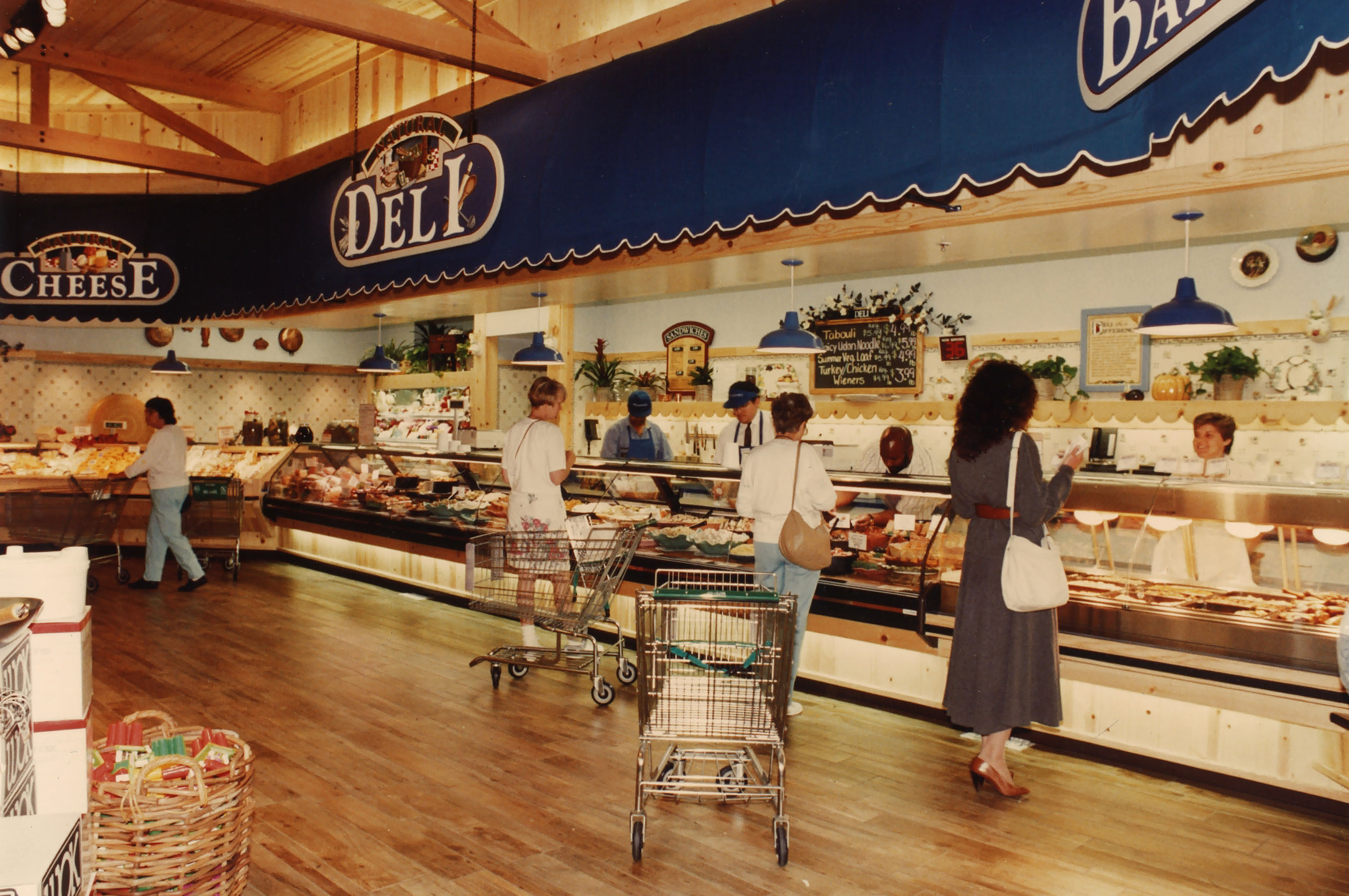 Interior of grocery store deli counter with several customers and workers