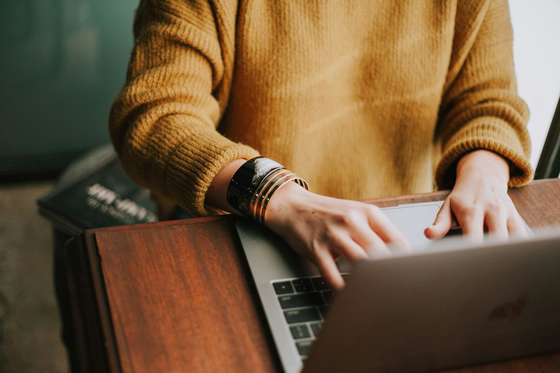 Arms wearing a wide bangle bracelet typing on a laptop keyboard