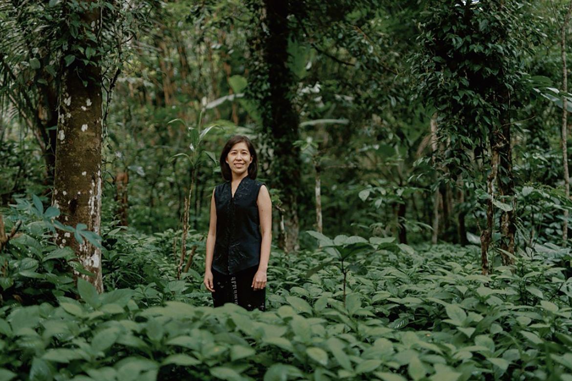 Denica Riadini-Flesch, wearing black, surrounded by foliage as she stands in a cotton field