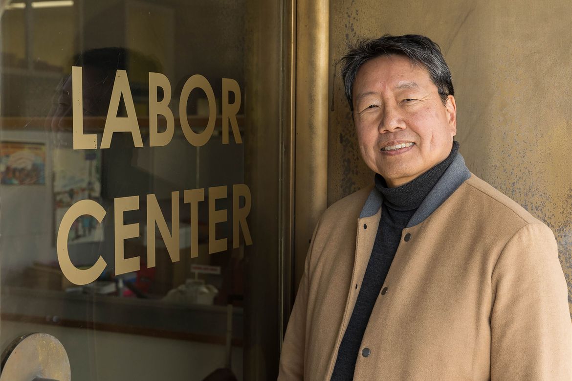 Kent Wong, in tan and gray jacket, standing next to glass door with Labor Center printed on it
