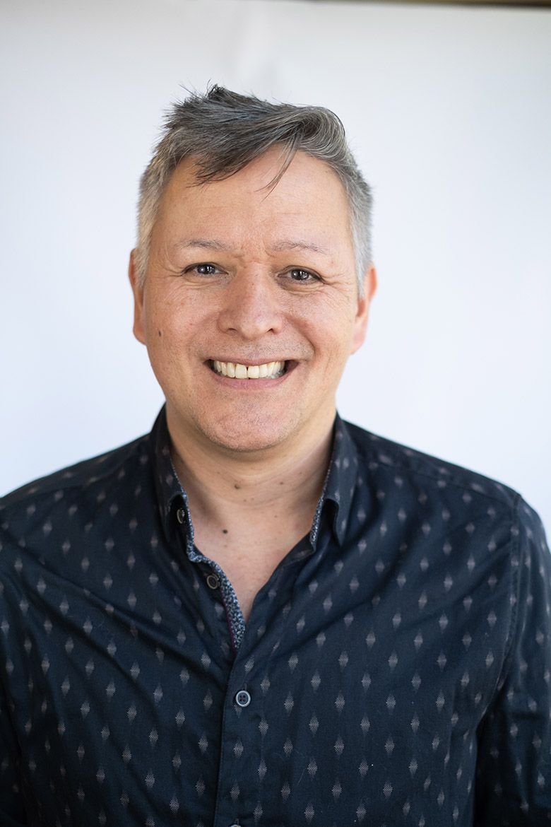 Headshot of Sean Metzger, smiling, wearing a dark patterned button-down shirt against a light background, with a navy blue panel on the left side of the image.