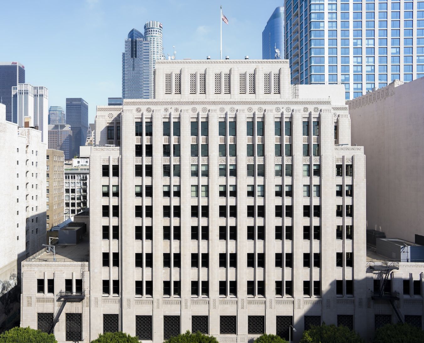 Exterior view of UCLA Downtown, a historic Art Deco building on Spring Street in downtown Los Angeles. The limestone façade features decorative architectural details, with modern skyscrapers rising behind the building beneath a clear blue sky.