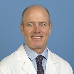 Headshot of S. Thomas Carmichael in a white lab coat and tie, smiling in front of a blurred indoor background.