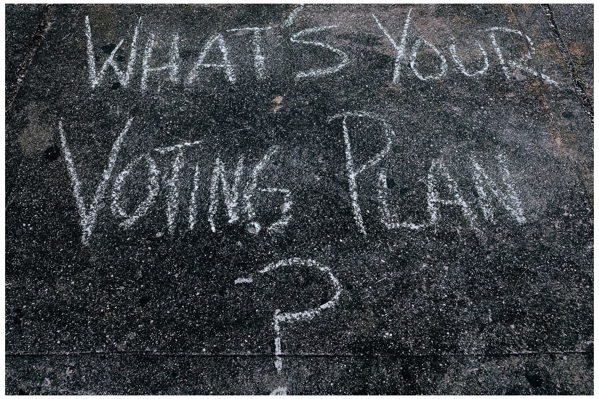 The question 'What's your voting plan?' written in white chalk on a dark pavement sidewalk."