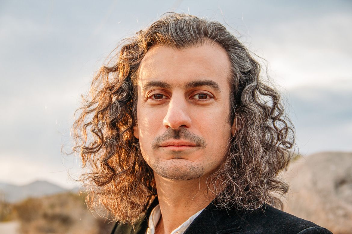 Portrait of Raffi Joe Wartanian outdoors against a cloudy sky and desert landscape.