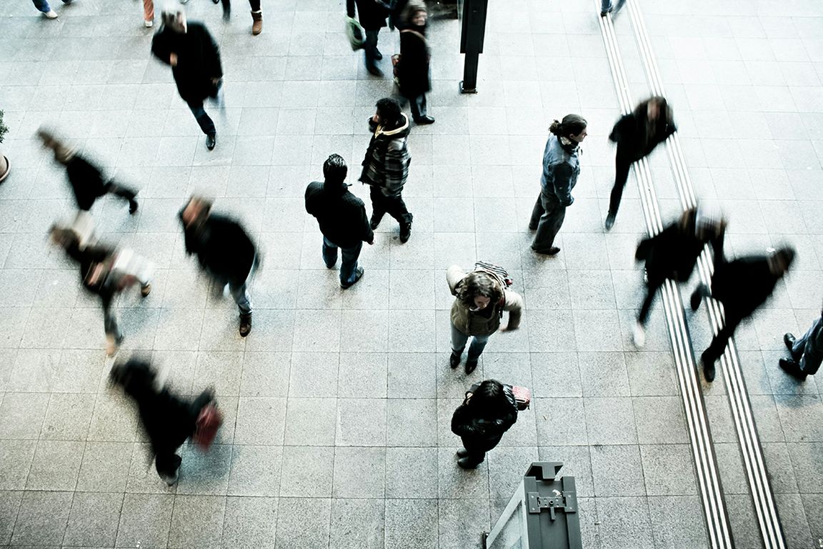 Aerial view of pedestrians walking across a large tiled plaza, with motion blur conveying the busyness of the crowd.