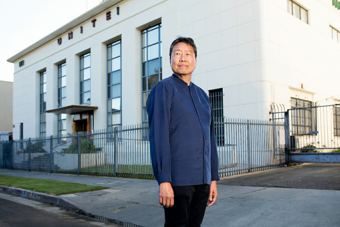 Kent Wong, in blue top and black pants, standing in front of a building that says UNITE!