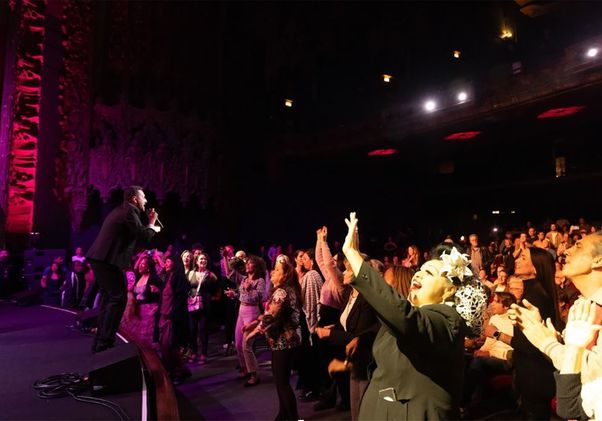Orquesta Akokán, in dark suit, performs onstage in front of a standing crowd 