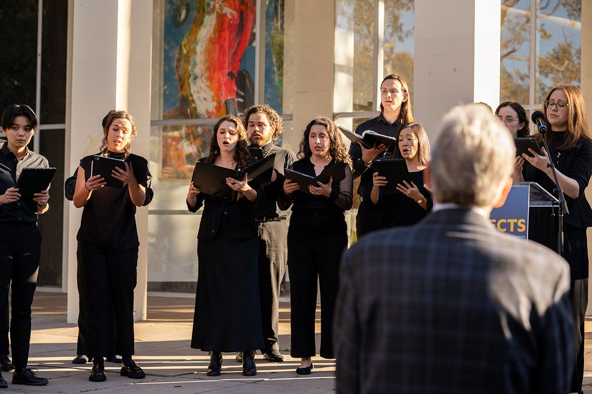 Members of the UCLA Chamber Singers, dressed in black, perform outdoors in front of the Schoenberg Hall columns at a UCLA Connects event marking the one-year anniversary of the LA fires.