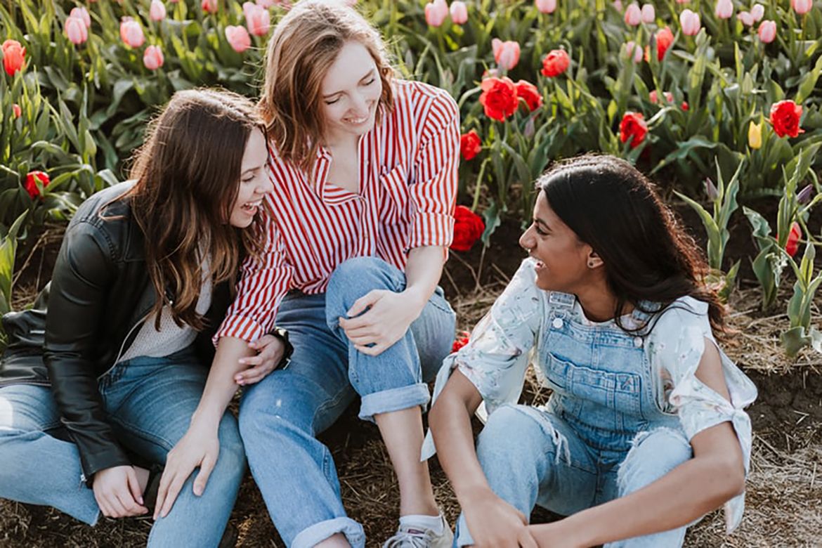 Photo | Three young women sit together laughing in front of a field of ...