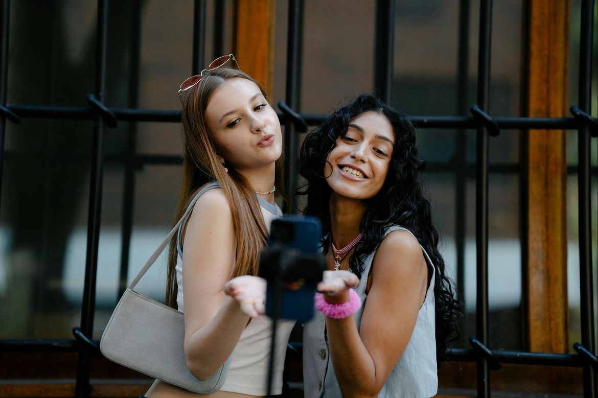 Two young women holding up a hand with palm facing up as they pose for a smartphone selfie