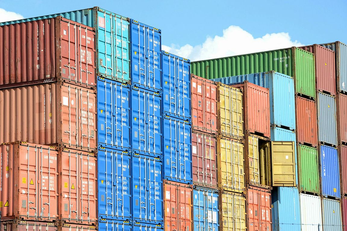 Stacks of multicolored intermodal shipping containers in blue, red, green, and yellow piled several stories high against a partly cloudy sky.